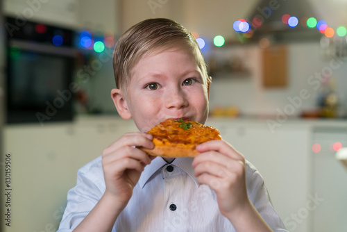 white baby child eats pizza sits at a table in the kitchen