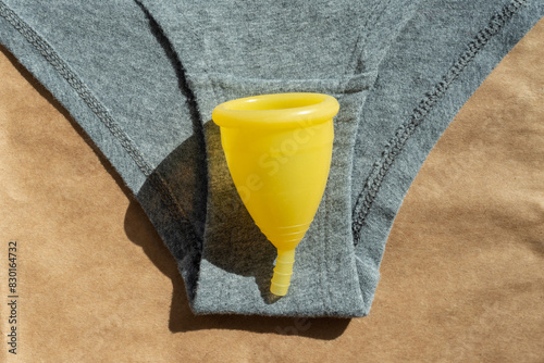 Women's gray cotton underwear and yellow menstrual cup on a paper natural background, top view, flat lay. Women's health concept. Environmentally friendly concept. Zero waste concept.