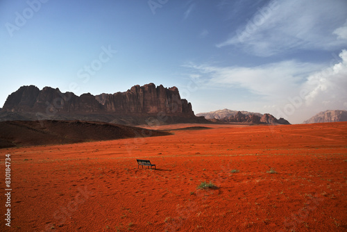 Ein Panorama des markanten Al Qattar Massiv in der Wüste des Wadi Rum in Jordanien bei blauem Himmel und im Vordergrund sind die typischen Sanddünen die durch eine Regen rötlich leuchten.