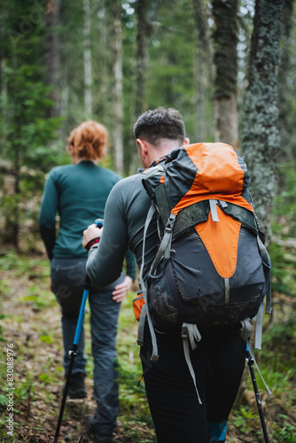 Young couple enjoying a hiking adventure in lush green forest with backpacks and hiking poles. Exploring nature, trekking through woodland, and escaping into the serene wilderness