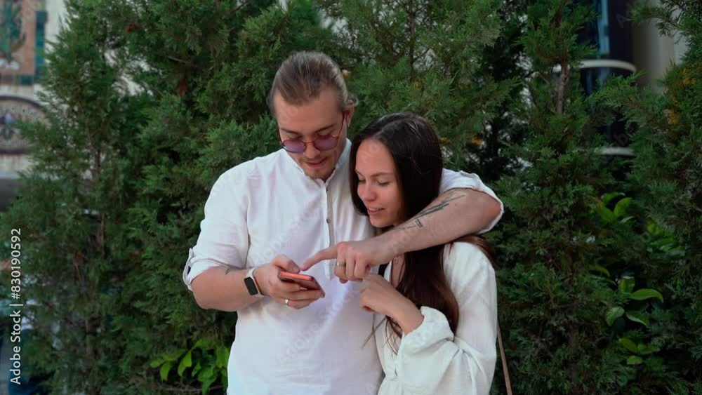 Young couple using smartphone outdoor downtown. Cheerful young woman and man using mobile phone. Social media, messenger, mob app, watching video, reel, online shopping, browsing internet.