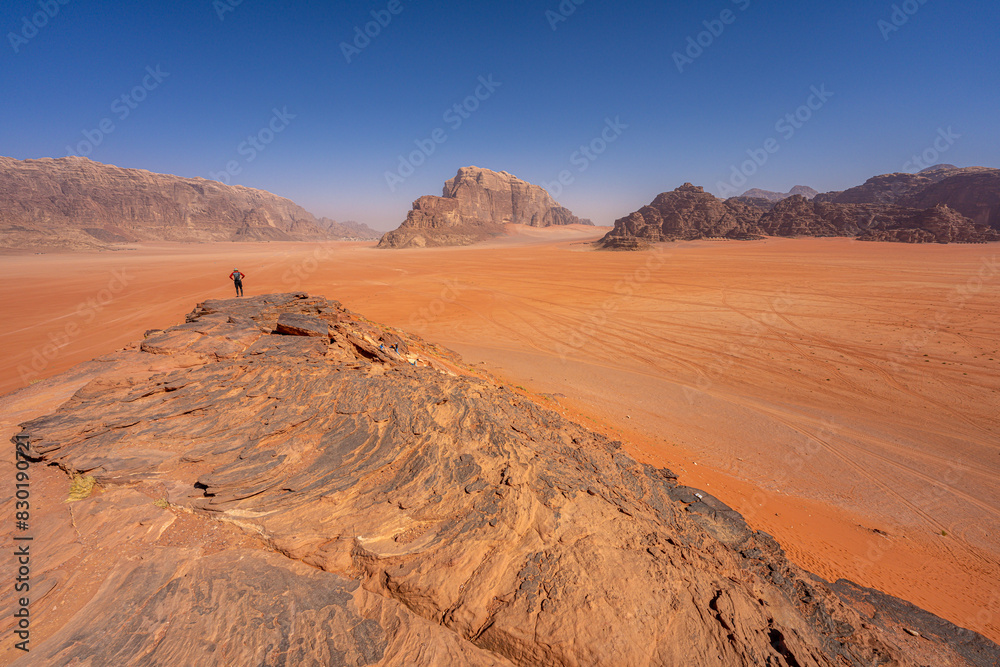 Fototapeta premium Majestic Desert Valley in Wadi Rum, Jordan: Expansive Red Sands and Towering Sandstone Cliffs Under Clear Blue Sky