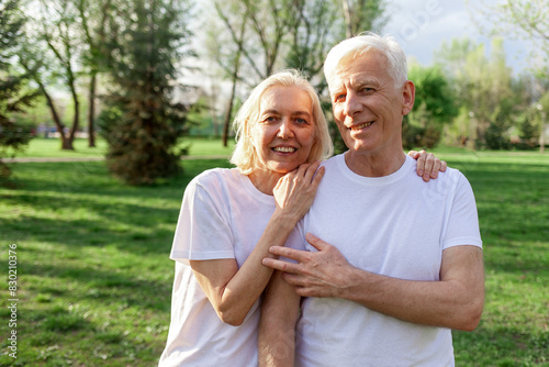 elderly couple of seniors man and woman hugging and smiling in the park outdoors, gray-haired grandparents in white T-shirts in nature © Богдан Маліцький