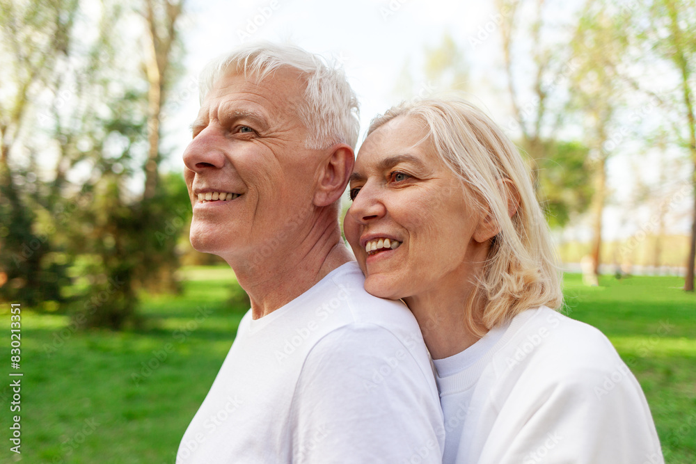elderly couple of seniors man and woman hugging and smiling in the park outdoors, gray-haired grandparents in white T-shirts in nature