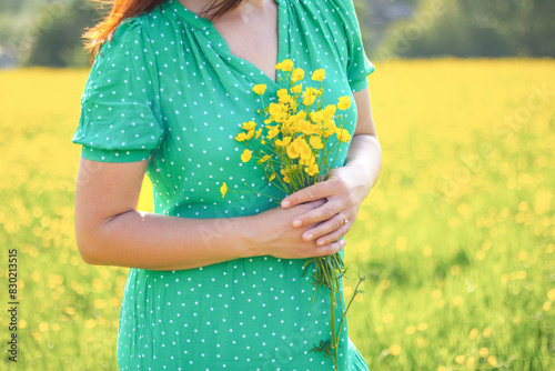 woman wearing a green dress holds yellow flowers in the hands, crop, no face