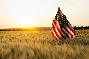 Young happy woman with American flag in a wheat field at sunset celebrate Independence day. 4th of July. Patriotic holiday, american day. Independence Day.