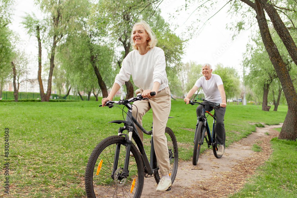 Obraz premium elderly senior couple rides bicycle in the park in the summer and smiles, old gray-haired man and woman are actively resting outdoors, old people practice cycling in forest