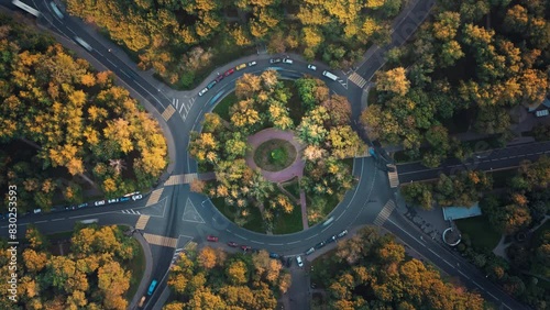 Top down time-lapse aerial view of a park with a roundabout intersection with slow camera rotation, beautiful sunset illuminates trees. Cars move fast along the road during an autumn traffic jam.