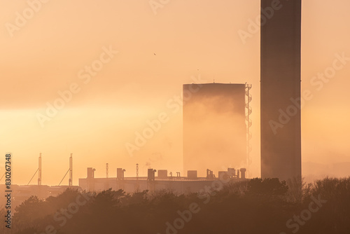 Tall chimney in front of the sun in locally dense fog. © Trygve