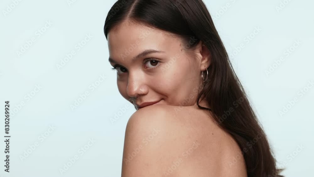 Portrait of a flirty young woman glancing playfully over her shoulder against a soft blue background. Portrait of a flirty young woman glancing playfully over her shoulder against a soft blue background.