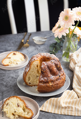 French Klouglof in a plate with its sliced piece, flowers in background. It's a cake traditionally baked in a distinctive ring pan, similar to Bundt cake, but leavened with baker's yeast.