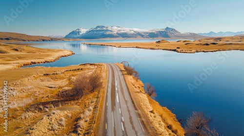 Aerial view of a serene fjord with a winding road, surrounded by mountains and golden grasslands under a clear blue sky. photo