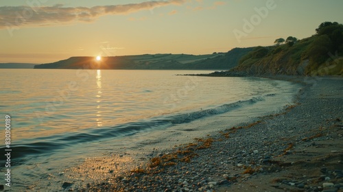 A serene sunset at Grota Beach in Portugal  with the sun casting a warm glow over gentle waves and a pebbly shore.