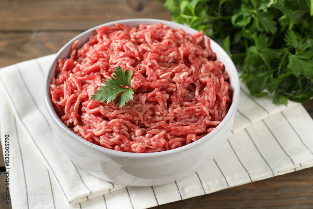 Raw ground meat in bowl and parsley on wooden table, closeup Raw ground meat in bowl and parsley on wooden table, closeup