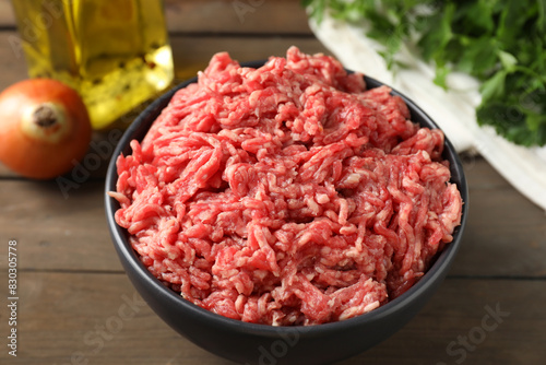 Raw ground meat in bowl on wooden table, closeup