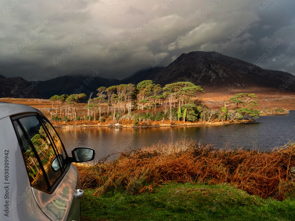 Φωτογραφία Side of silver car parked off road, stunning scenery of Connemara with lake, island, mountains and dramatic sky in the background