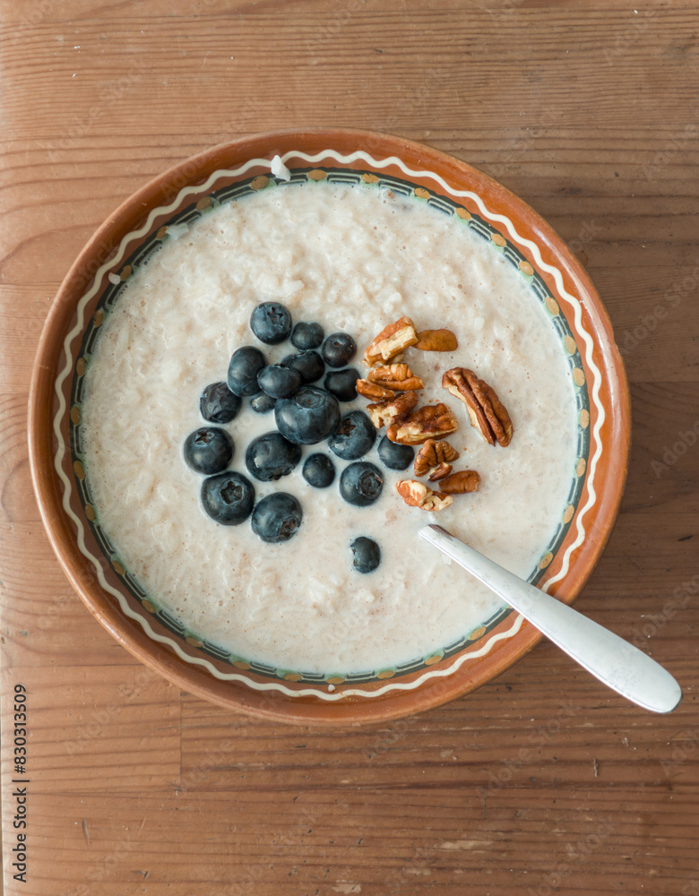 Healthy breakfast meal: Oatmeal porridge with white rise, vaccinium corymbosum berries and pecan nuts in a bowl plate with spoon