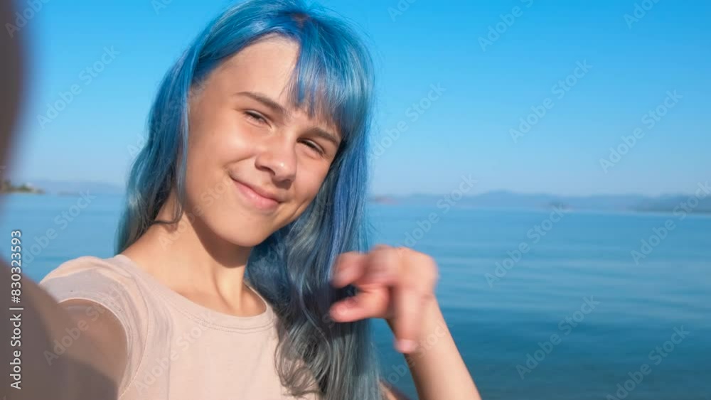 Blue girl posing in front of phone camera. A nice modern teen with blue hair have fun with her phone on the seashore. Blue girl posing in front of phone camera. A nice modern teen with blue hair have fun with her phone on the seashore.