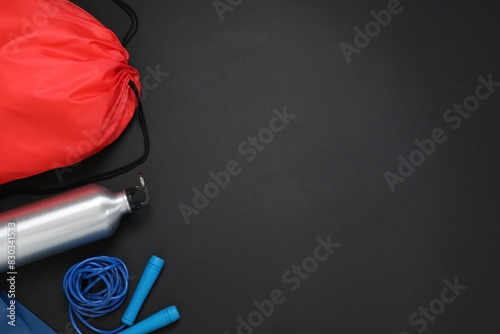 Red drawstring bag, skipping rope and thermo bottle on black background, flat lay. Space for text photo