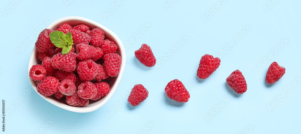 Bowl with fresh raspberries and mint on blue background Bowl with fresh raspberries and mint on blue background