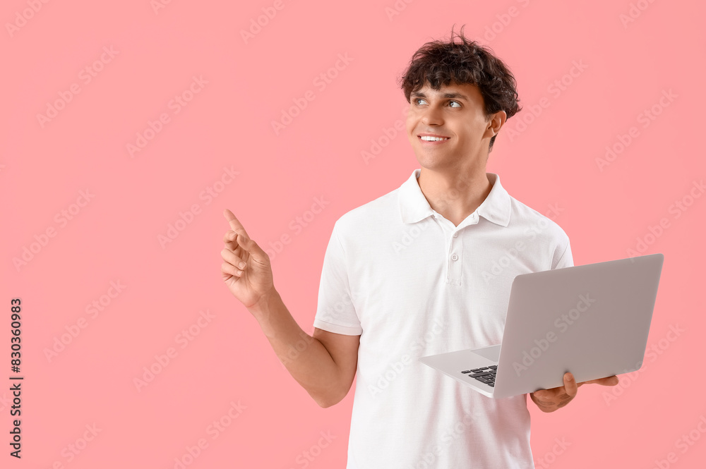 Male programmer with laptop pointing at something on pink background