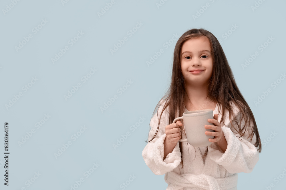 Cute little happy girl in bathrobe with cup of tea on blue background Cute little happy girl in bathrobe with cup of tea on blue background