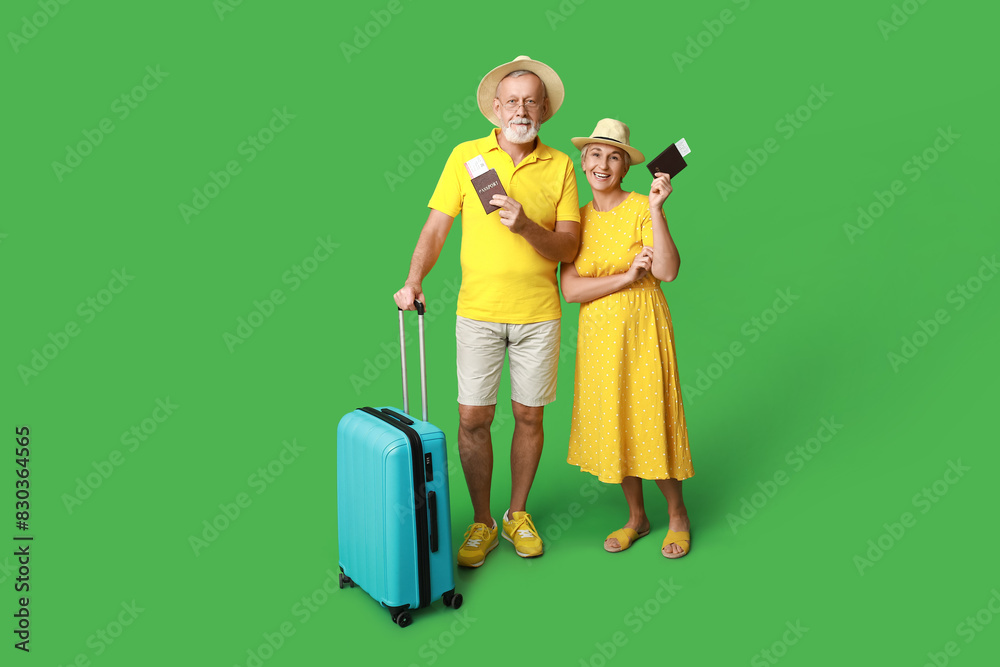 Mature couple of travelers with passports and suitcase on green background Mature couple of travelers with passports and suitcase on green background