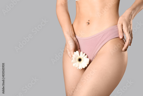 Young woman in panties with beautiful white flower on grey background © Pixel-Shot