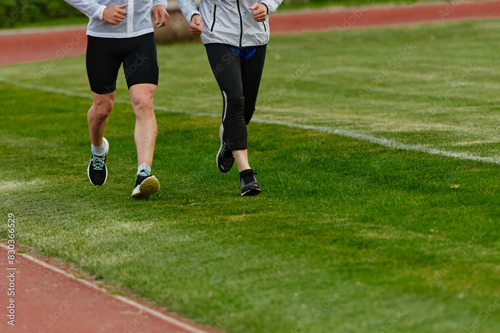 Obraz premium An inspiring and active elderly couple showcase their dedication to fitness as they running together on a lush green field, captured in a close-up shot of their legs in motion.