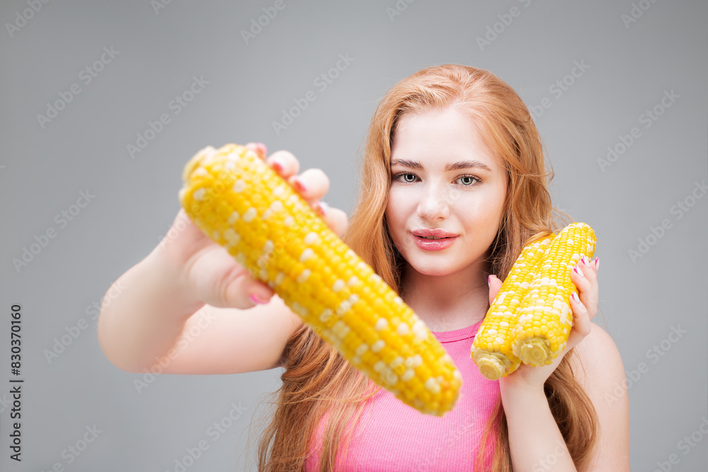 Happy young woman holding a head of corn isolated on gray background. Healthy eating concept. Diet. Happy young woman holding a head of corn isolated on gray background. Healthy eating concept. Diet.