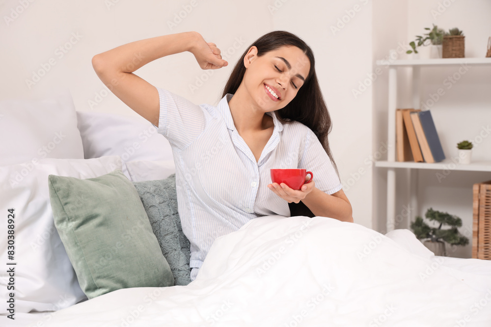 Pretty young woman with cup of hot coffee lying in bed at home