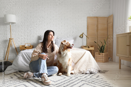 Young woman with Australian Shepherd dog sitting on floor in bedroom