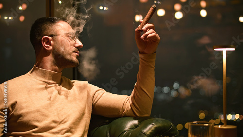 Businessman smokes cigar in restaurant. Media. Man smokes cigar in luxury restaurant at night. Elegant man smokes cigar in evening restaurant