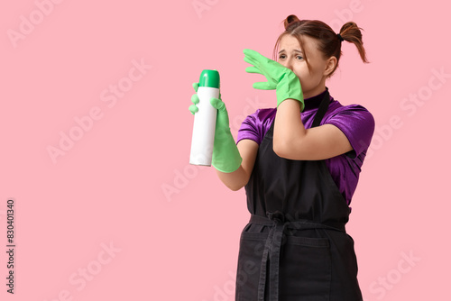 Young woman with air freshener covering her nose on pink background