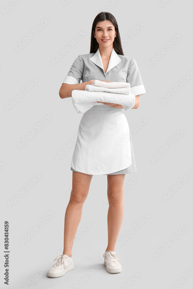 Young chambermaid with towels on light background Young chambermaid with towels on light background