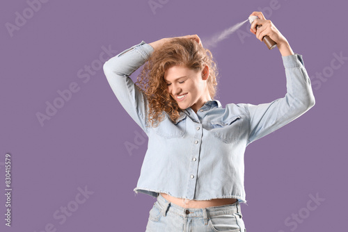 Young woman applying dry shampoo on her hair against violet background