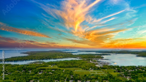 his breathtaking drone shot captures the serene beauty of Southold in The Hamptons, New York. As the sun sets, it casts a golden glow over the lush landscapes and the expansive waters of Peconic Bay. 