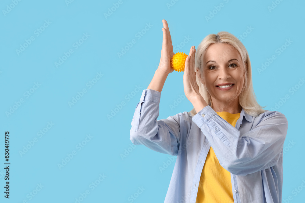 Mature woman massaging her hands with ball on blue background Mature woman massaging her hands with ball on blue background