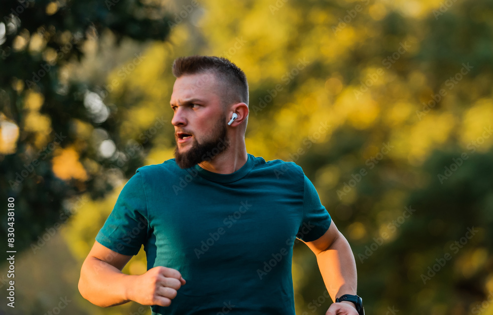 Young athletic man running or jogging at the park listening to music on wireless headphones active healthy lifestyle.