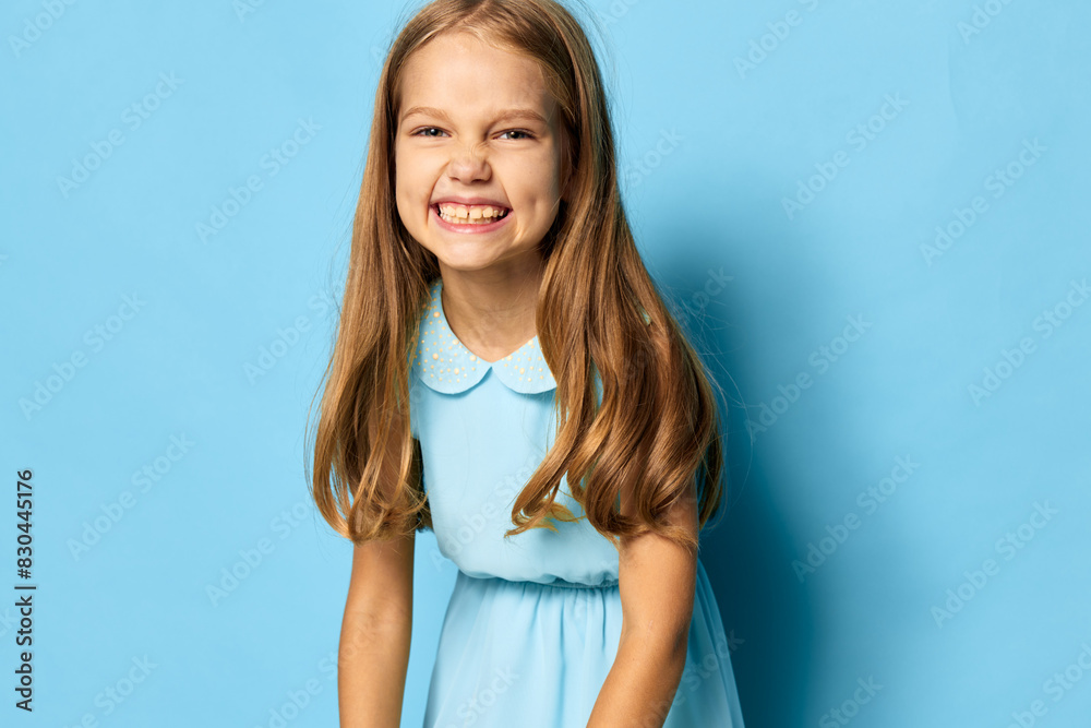 Little girl in a blue dress sitting on the floor with hands on knees, looking thoughtful and serene
