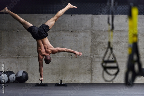 A muscular man in a handstand position, showcasing his exceptional balance and body control while performing a variety of exercises to enhance his overall body stability and strength in a modern gym photo