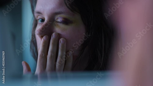 Close up shot of a young and scared Woman looking at her injured and bruised eye in the mirror with horror in her eyes in slow motion. photo