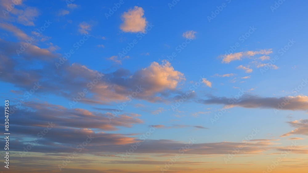 Obraz premium A serene sunset sky with scattered clouds reflecting warm tones of orange and pink. The deep blue sky contrasts beautifully with the soft colors of the clouds, creating a tranquil scene. 