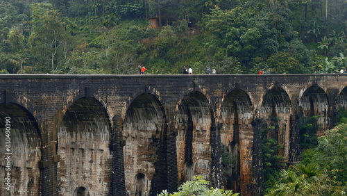 Tourists walk on stone bridge in jungle. Action. People walk on ancient stone bridge in rainforest. Beautiful landscape with people on aqueduct and green hills