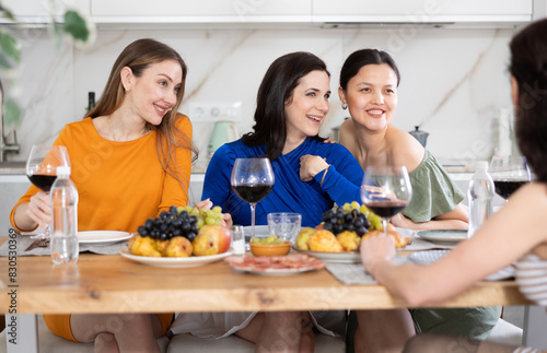Casual evening where group of cheerful carefree besties sharing wine, dining together, and chatting in cozy home kitchen ..