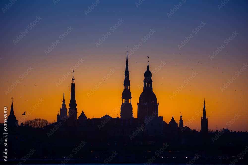 A beautiful cityscape of Riga, Latvia during sunrise. Church towers against colorful sky. City panorama in morning with buildings.