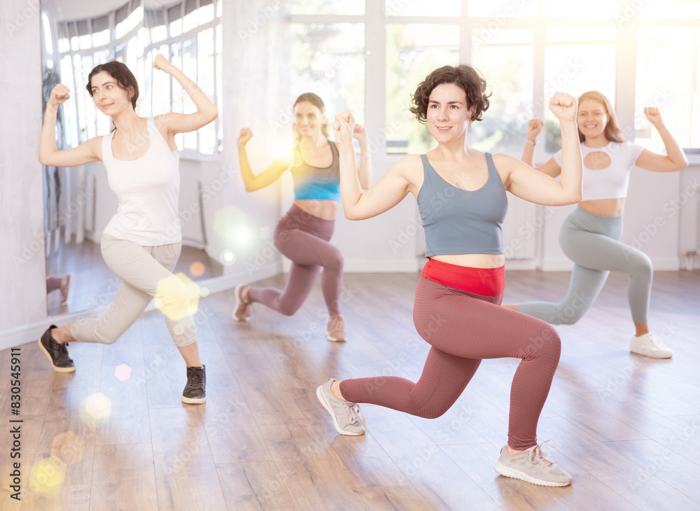 Fototapeta premium Cheerful emotional sporty young Latina rehearsing popping techniques during group workout in modern street dance studio
