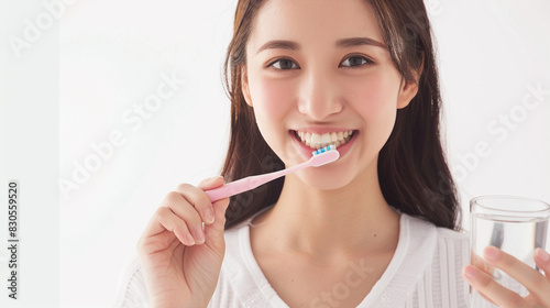 beautiful Japanese woman brushing her teeth  smiling at the camera  holding a glass of water in one hand  white background  high resolution photography  stock photo  in the style