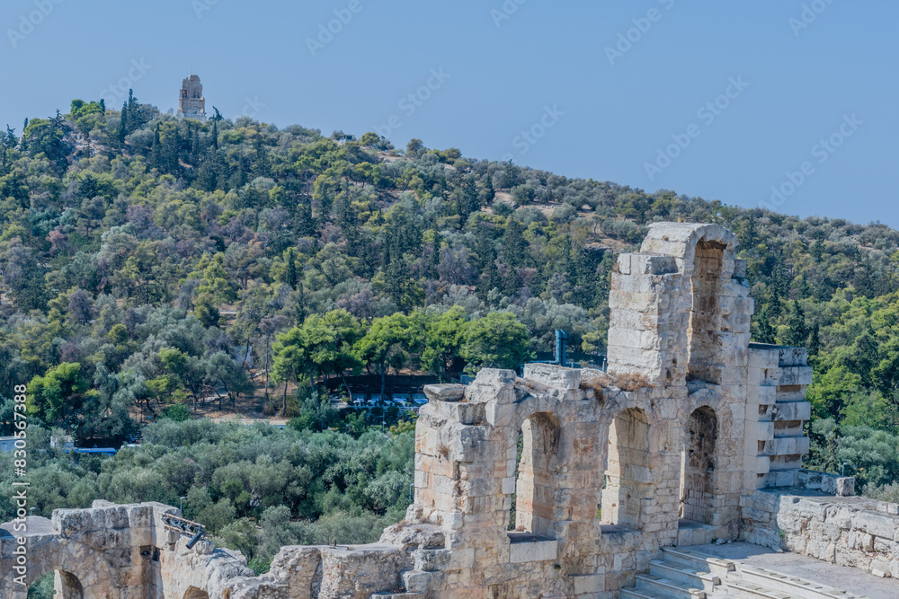 Ancient theatre ruins set against a backdrop of a forested hill and a clear sky, in Athens, Greece