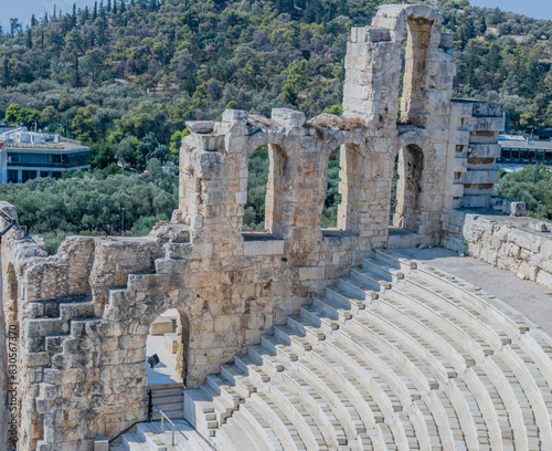 Stone steps of an ancient theatre surrounded by greenery and historical ruins, in Athens, Greece